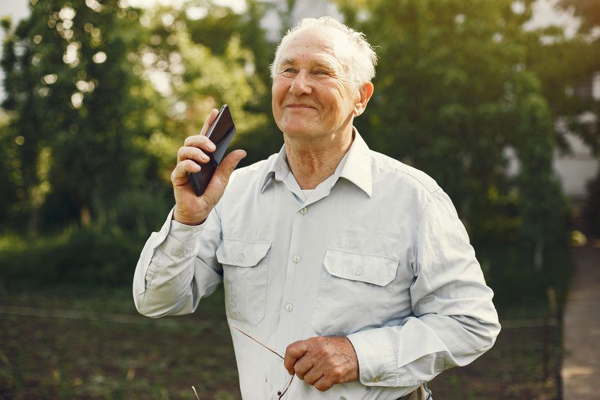 An older man smiling in his garden as he takes a call on his mobile