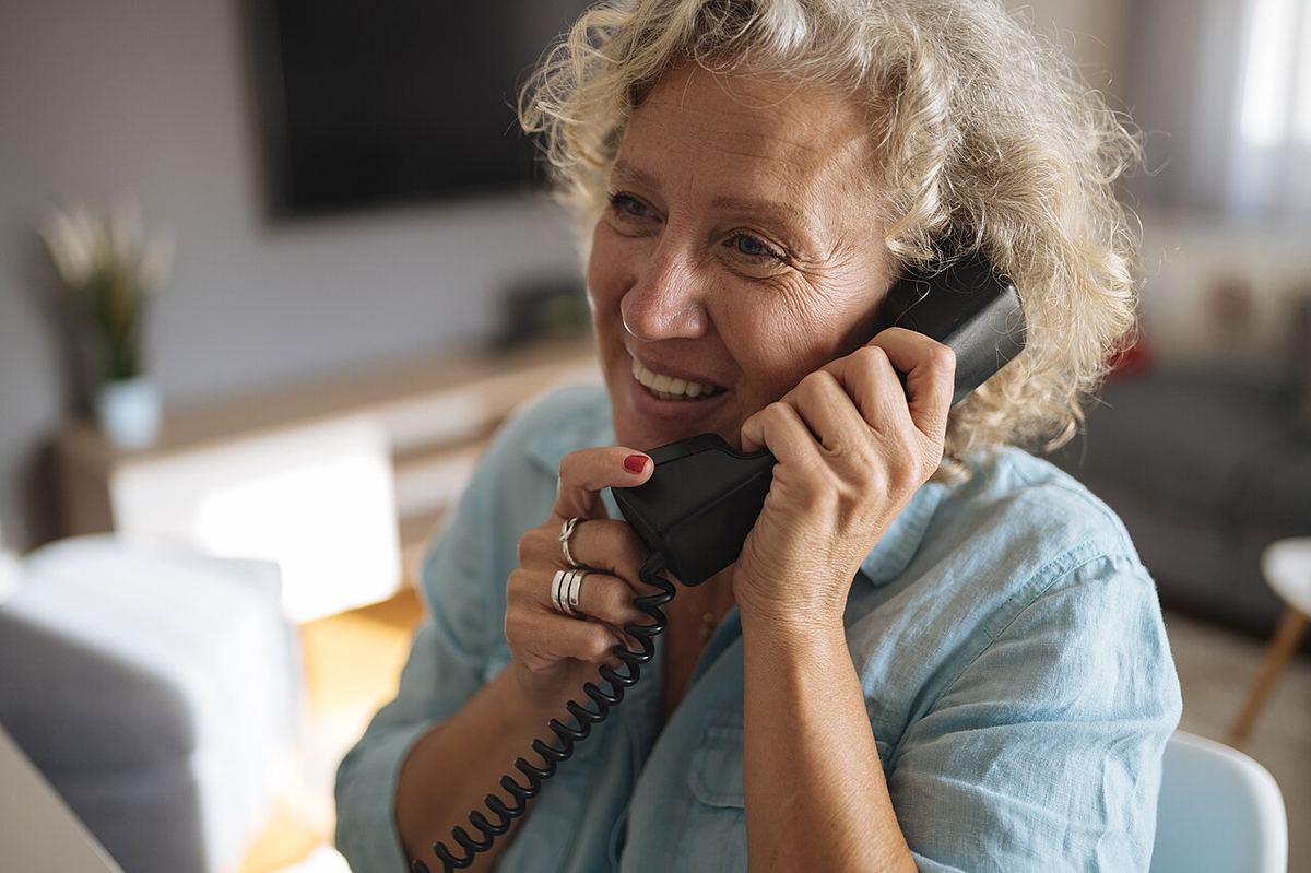 An older woman laughing as she talks on her home phone